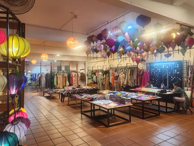A shop interior with dozens of colorful silk lanterns hanging, clothing racks and fabric tables