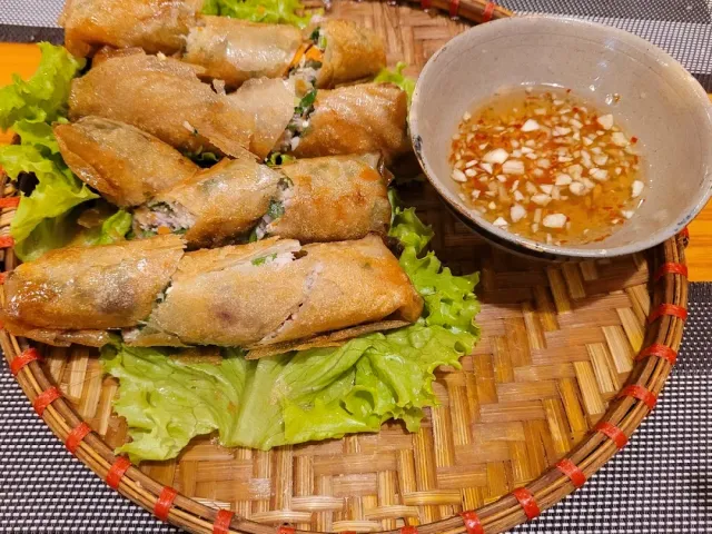 A cluster of fried rolls on lettuce leaves in a straw tray beside a bowl of sauce