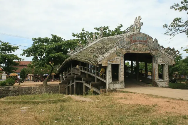 A covered wooden bridge with a tiled roof over a village canal