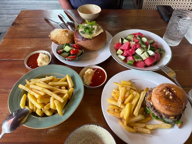 A wooden table with a burger, fries, a stuffed bread roll and a watermelon and cucumber salad
