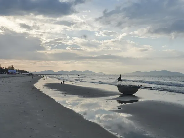 A wide sandy beach with a round basket boat under a cloudy sunset sky