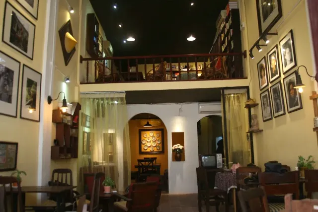 A two story space with a wooden gallery, cream walls full of framed pictures and wall lamps