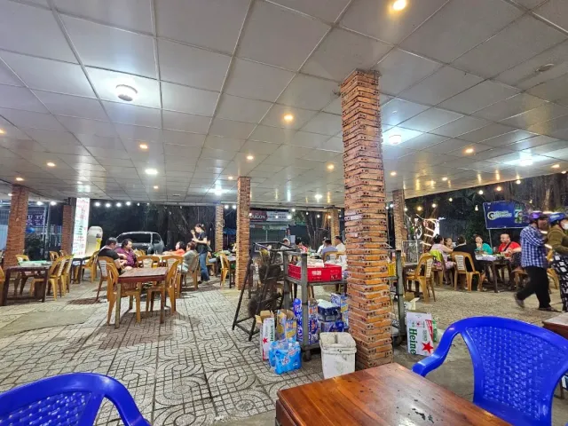 A covered seating area in the evening with a brick pillar, wooden tables and blue plastic chairs