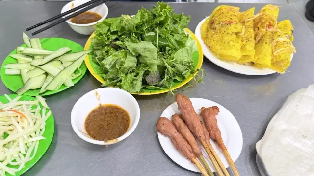 Plates with leafy greens, cucumber, crisp yellow pancakes and meat skewers on a metal table