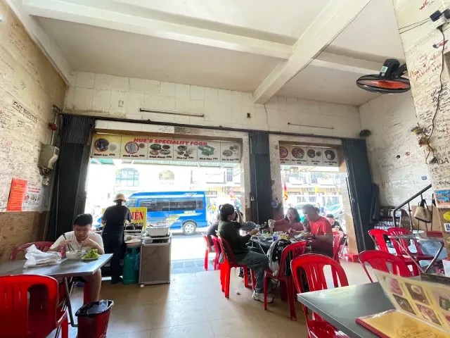 A plain eatery with walls covered in signatures, red plastic chairs and a front open to the street