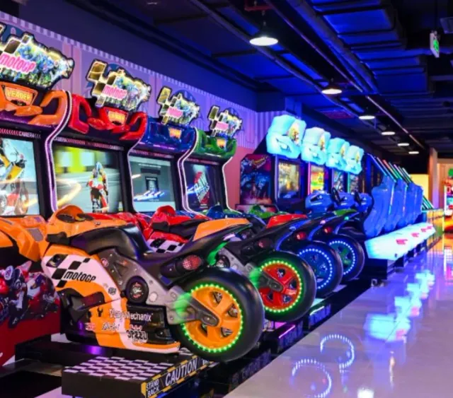 An arcade hall with a row of colorful motorcycle racing machines and neon lighting