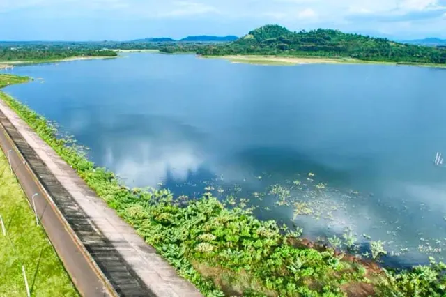 A wide blue body of water with a concrete embankment along the bank and green vegetation