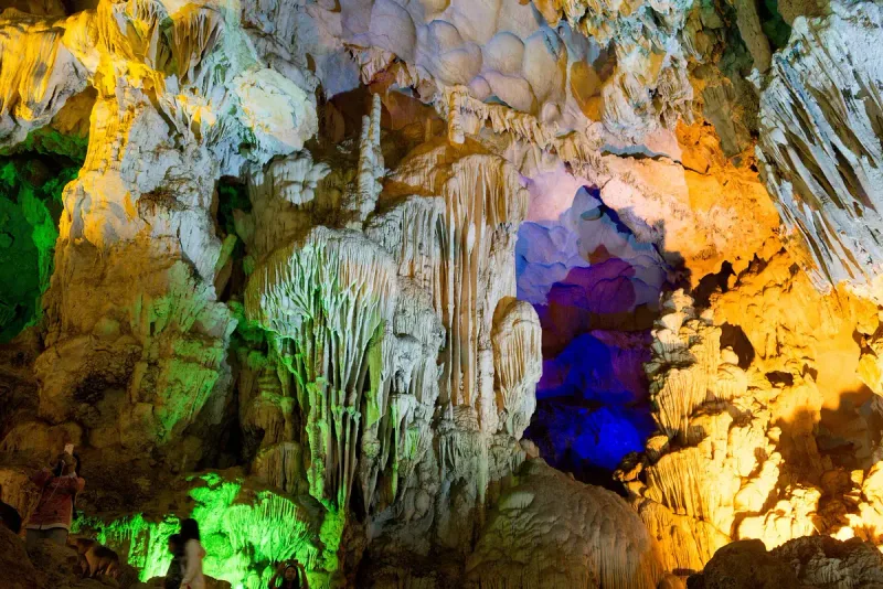 Stalactites and columns lit in green, blue and yellow inside Thien Cung Cave in Ha Long Bay