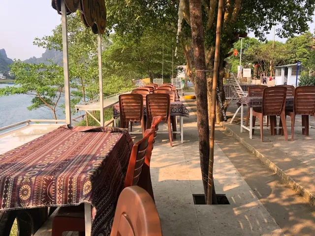 A riverside terrace with a patterned cloth, stacked plastic chairs and rock peaks behind