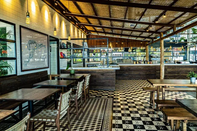 A bar with a chequered floor, wicker chairs and shelves of bottles