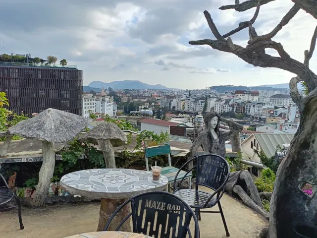 A terrace with concrete mushroom sculptures, metal chairs and a view over the city rooftops and hills