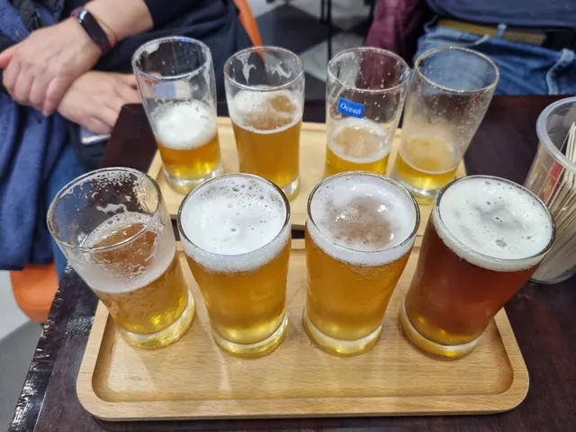 A wooden tray with eight glasses of beer in different shades on a table