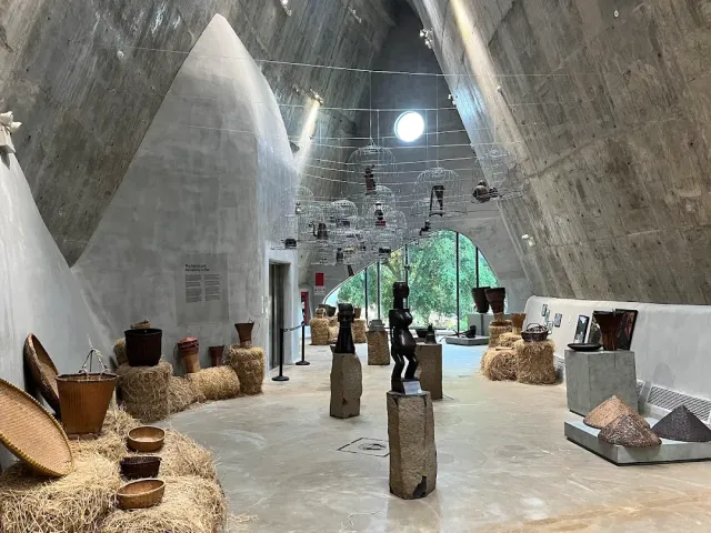 A high curved concrete hall, exhibits on plinths and straw bales on the floor