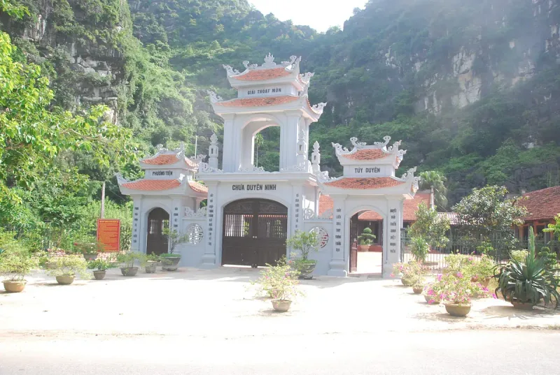 The white entrance gate of Duyen Ninh Pagoda with its three roofs, and the wooded karst cliffs of Hoa Lu above