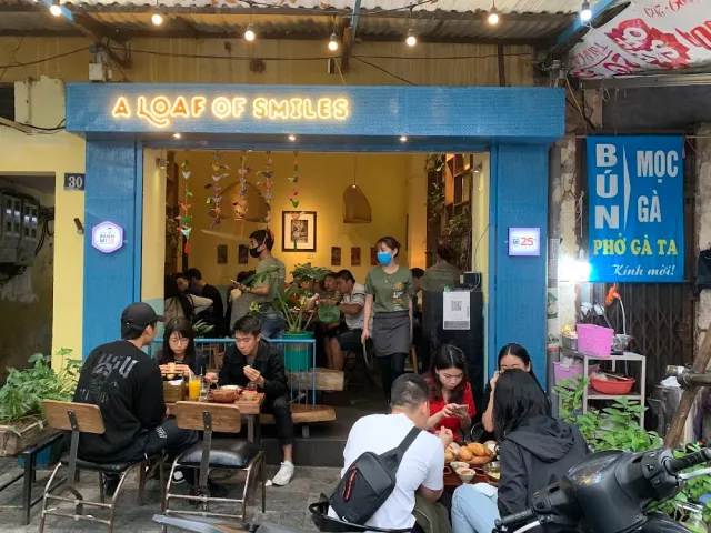 A blue storefront with a lit sign, diners at low wooden tables on the sidewalk