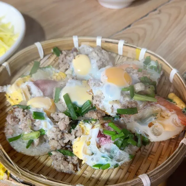 A bamboo basket of small pancakes topped with egg, minced meat and green onion