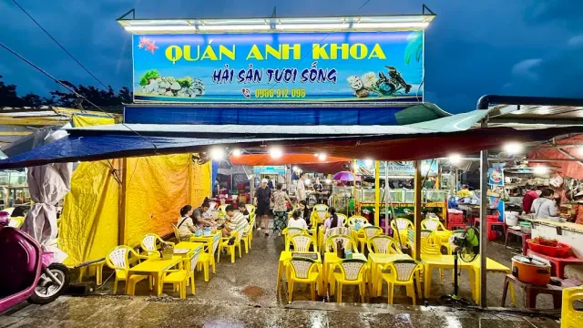 A lit eatery at night with rows of yellow plastic chairs and diners at the tables