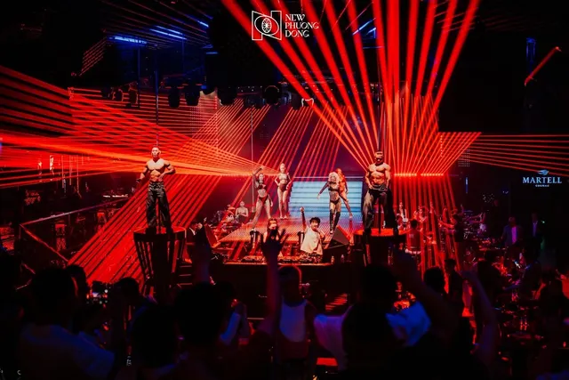 Red laser beams above a stage with dancers and a large crowd in a dark club