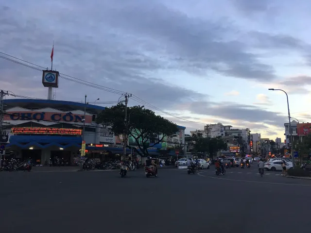 The street in front of a market at sunset with traffic and scooters
