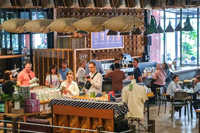 An industrial roastery hall with lamps shaped like bean sacks and customers by a product stand