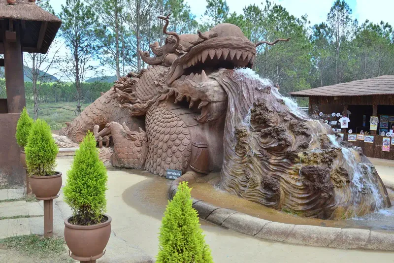 A giant dragon sculpted from reddish clay with water running over carved waves, among pine trees