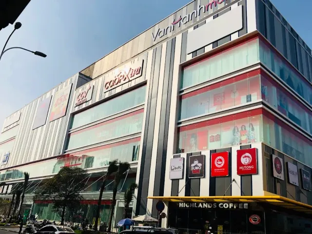 A glass and metal facade of a modern shopping centre, brand signs and a cafe below