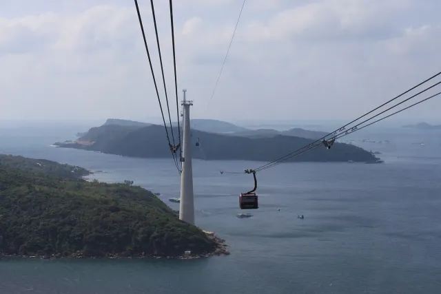 A cable car pylon and cables above blue water and a green island