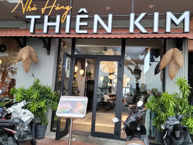 A restaurant front with a white lettered sign, woven lampshades, potted plants and parked motorbikes
