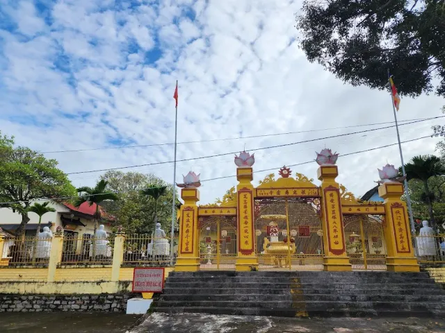 A gilded yellow gate with lotus finials, two flagpoles and flags above it