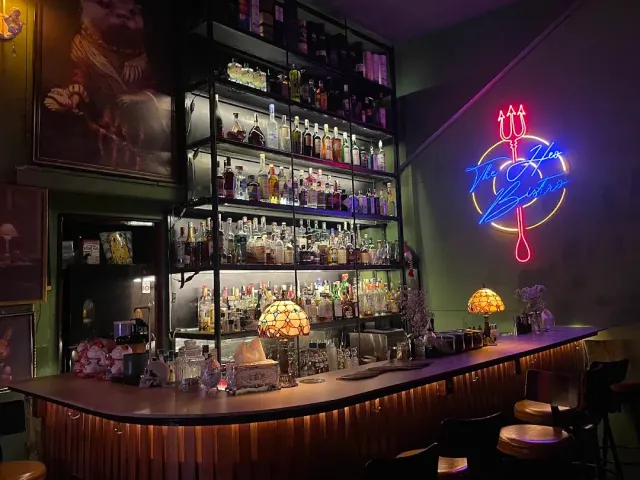 A curved wooden counter with bottle shelves, stained glass lamps and a neon trident sign