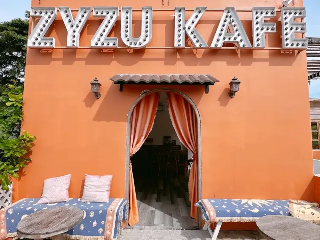 An orange building with bulb letters on the roof, an arched opening with curtains and cushioned benches