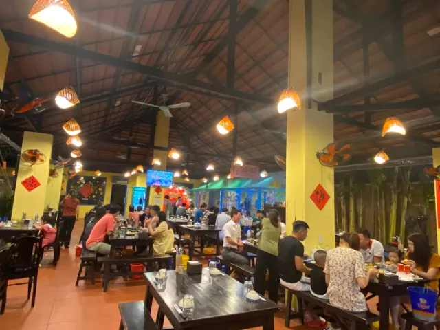 A large hall with a wooden ceiling, conical lampshades and fans, long tables full of diners