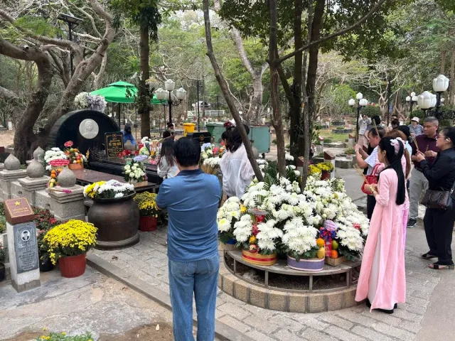 Many visitors around a round black headstone, white chrysanthemum wreaths and incense urns
