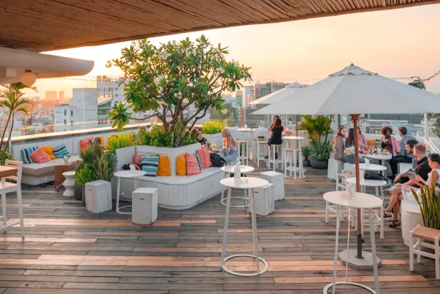 A wooden rooftop deck at sunset with white furniture, colorful cushions and a frangipani tree in the middle
