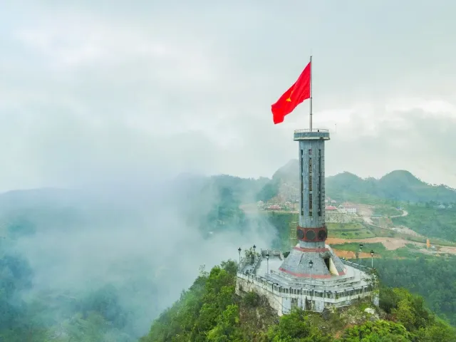 A stone tower on a summit among mists, with a red cloth bearing a star flying at its top
