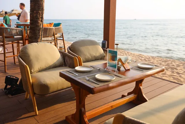 A set table with padded armchairs on a wooden deck, right by the sand and the sea