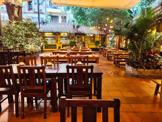 A tiled courtyard with dark wooden tables, lit food stalls in the background and palm trees