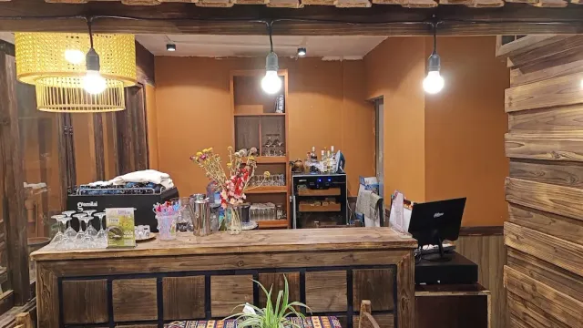 A rough wooden counter with hanging lamps, glasses, a flower vase and a register screen