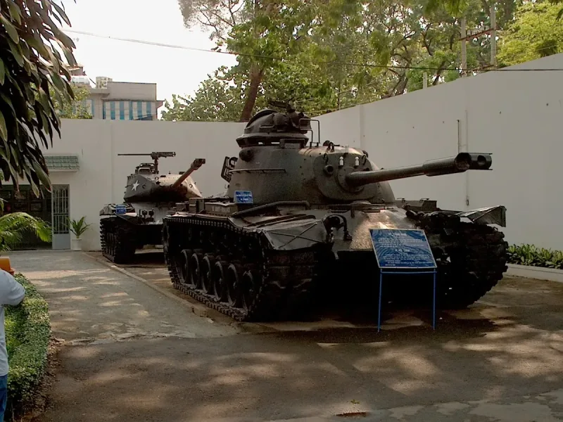 Two tanks in an outdoor display yard beside an information panel, under trees